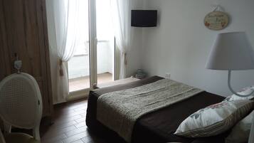 Hotellihuone, jossa on sänky, tuoli, televisio, lamppu ja pieni pöytä, jonka päällä on kaukosäädin.
