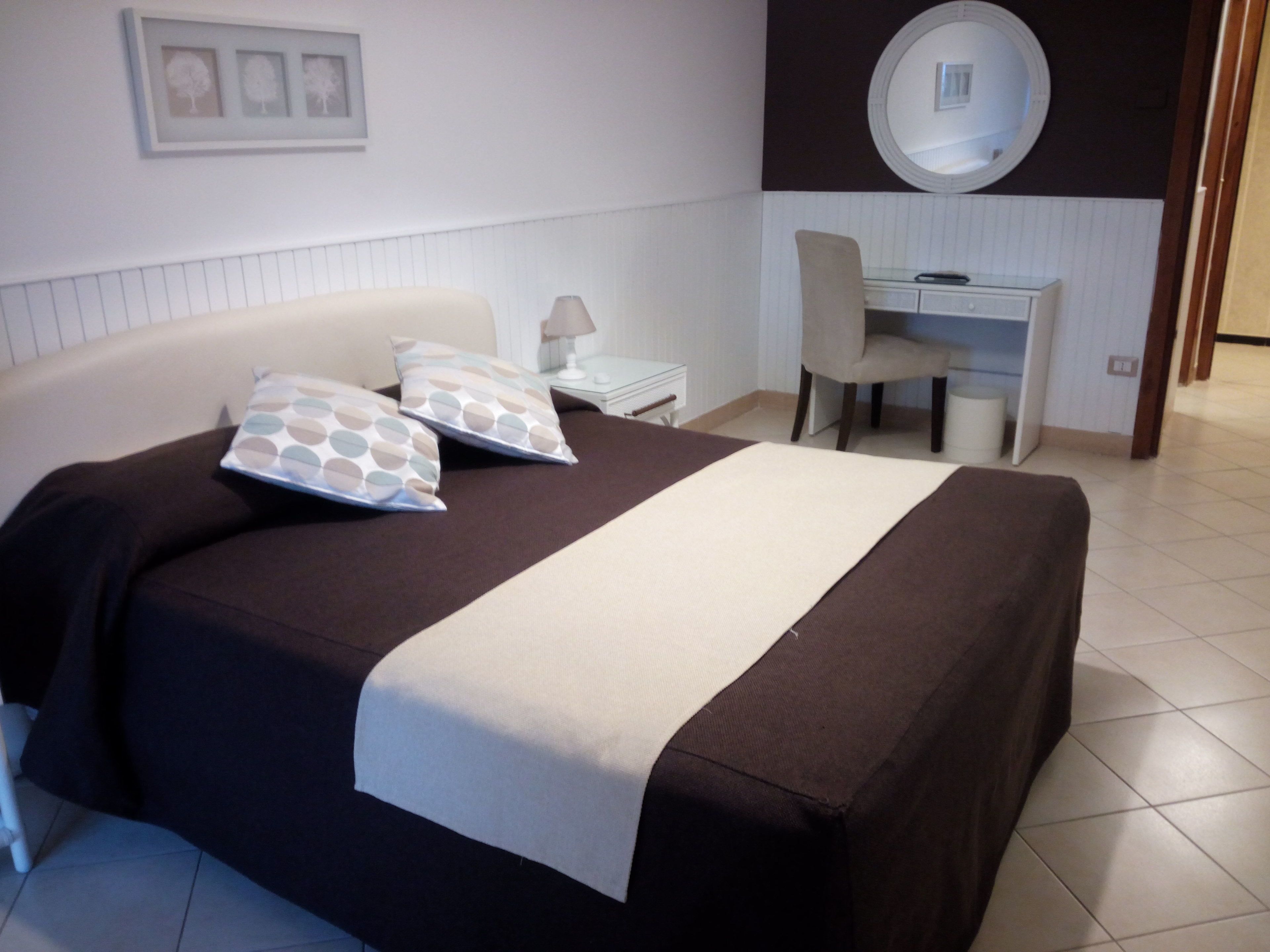 A bedroom with a bed, bedside table, lamp, chair, and a desk with a mirror.