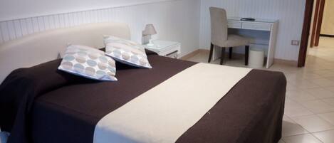 A bedroom with a bed, bedside table, lamp, chair, and a desk with a mirror.