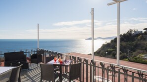 A terrace with outdoor seating, a table with drinks, and a view of the sea and hills. - Mini Hotel (Pozzuoli)