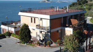 A two-story building with a red roof, a balcony, and a view of the sea. - Mini Hotel (Pozzuoli)