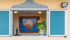 A doorway with a blue tiled wall, a decorative tile with a diamond shape, a potted plant with a flower, and a bottle on a tray. - Riviera B&B Rooms and Apartament SEA-VIEW (Maiori)