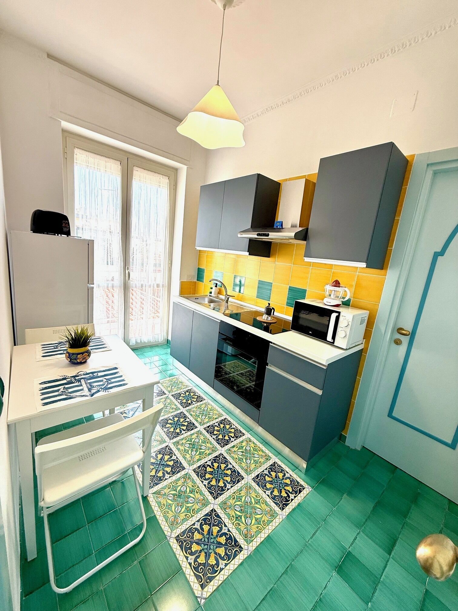 Een kleine keuken met een witte tafel, een magnetron en een spoelbak.
