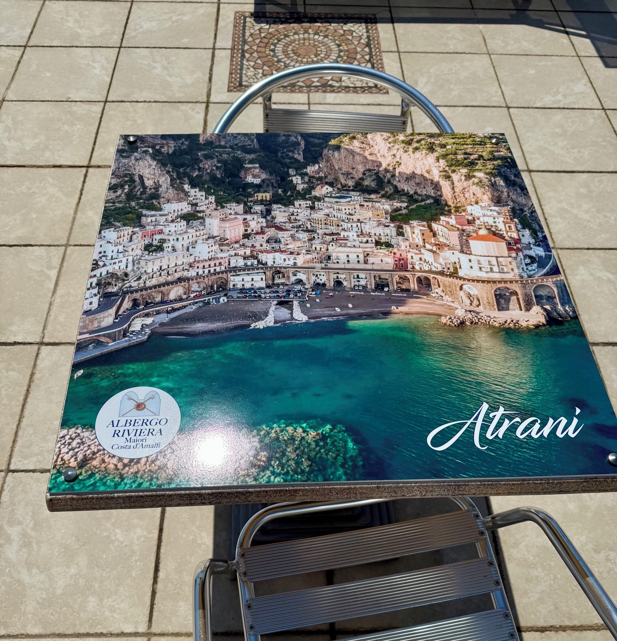 Uma mesa com uma impressão de uma cidade costeira, um logotipo e o nome 'Atrani'.
