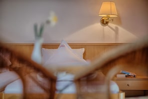 Ett hotellrum med en sänggavel i trä, en sänglampa, ett nattduksbord med en bok och ett par glasögon samt en kudde med hotellets logotyp.