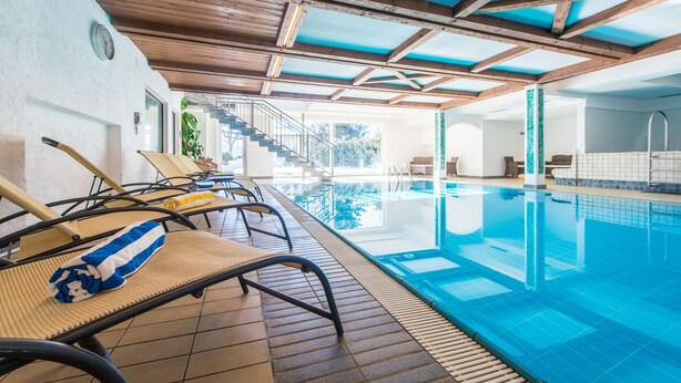 An indoor swimming pool with lounge chairs and a staircase leading to upper levels. - Gissbach (Brunico)