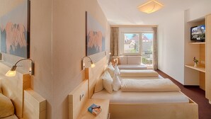 A hotel room with two beds, a TV, and a window with a view of buildings. - Gissbach (Brunico)