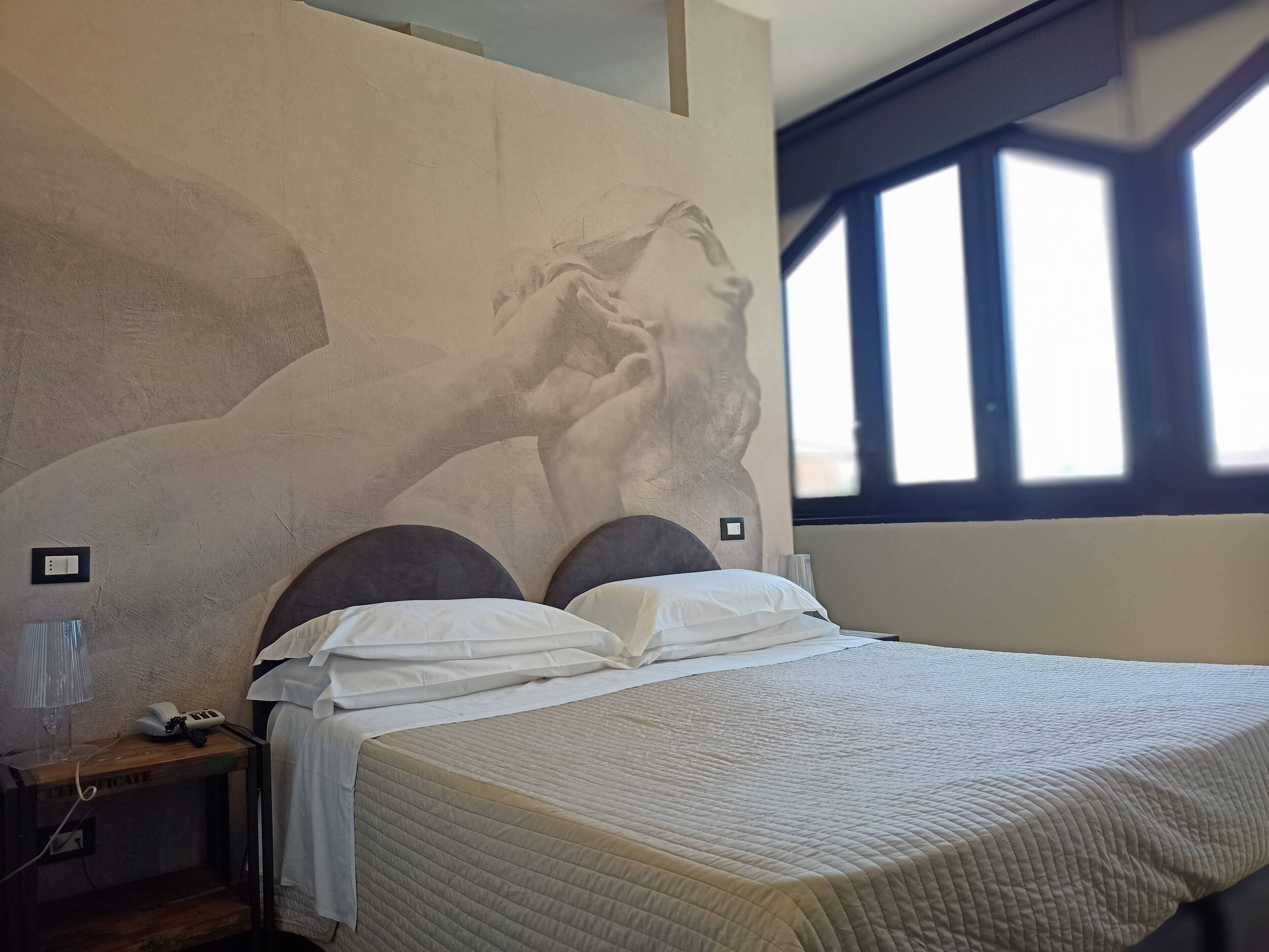 A bedroom with a large wall mural, a bed with white bedding, and a window with blinds.