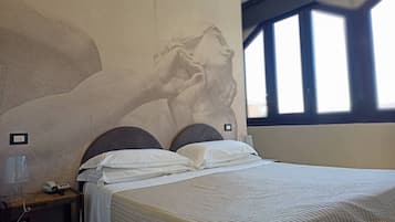 A bedroom with a large wall mural, a bed with white bedding, and a window with blinds.