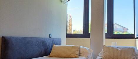 Habitación de hotel con dos camas, un ventanal grande y vistas al exterior.