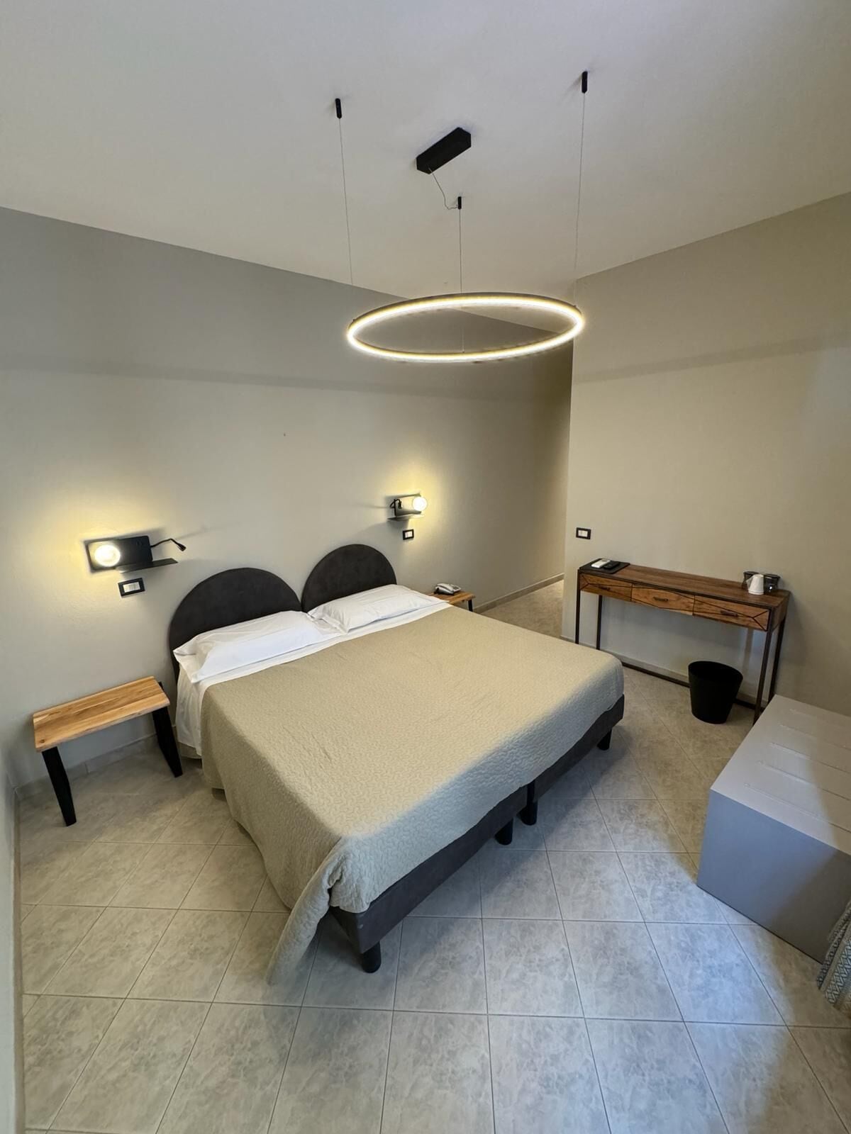 A modern bedroom with a large bed, bedside tables, a desk, and a circular ceiling light.