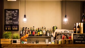 Zona de bar con una variedad de botellas de licor, un menú en la pizarra y lámparas colgantes.