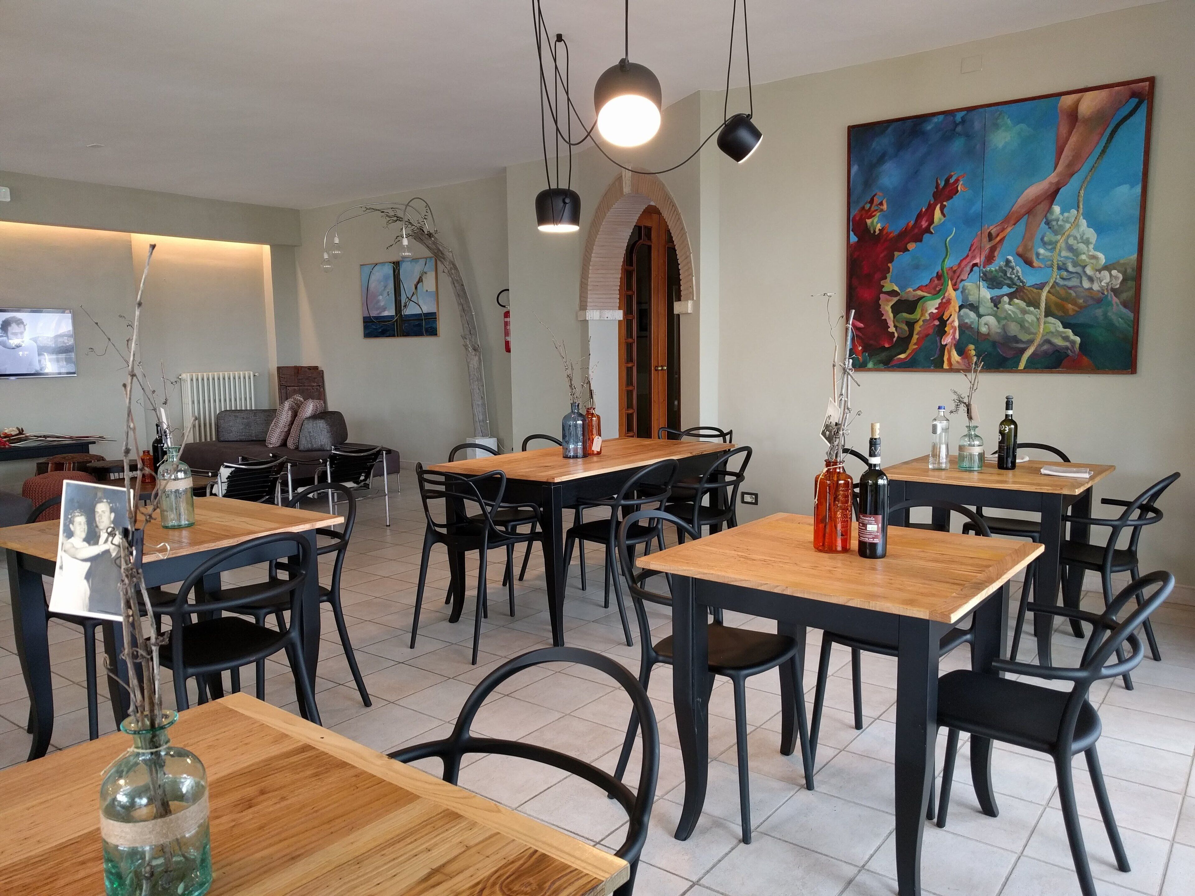 Un comedor con mesas de madera y sillas negras, un cuadro en la pared y un televisor al fondo.