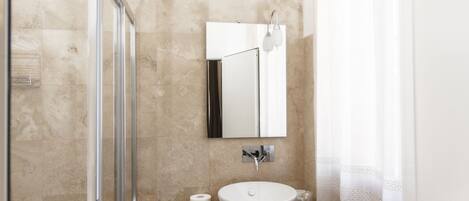 A bathroom with a glass shower enclosure, a sink with a mirror, and a towel rack.