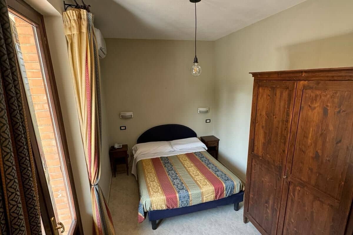 Une chambre à coucher comprenant un lit, une armoire en bois, une table de chevet et une lampe suspendue.