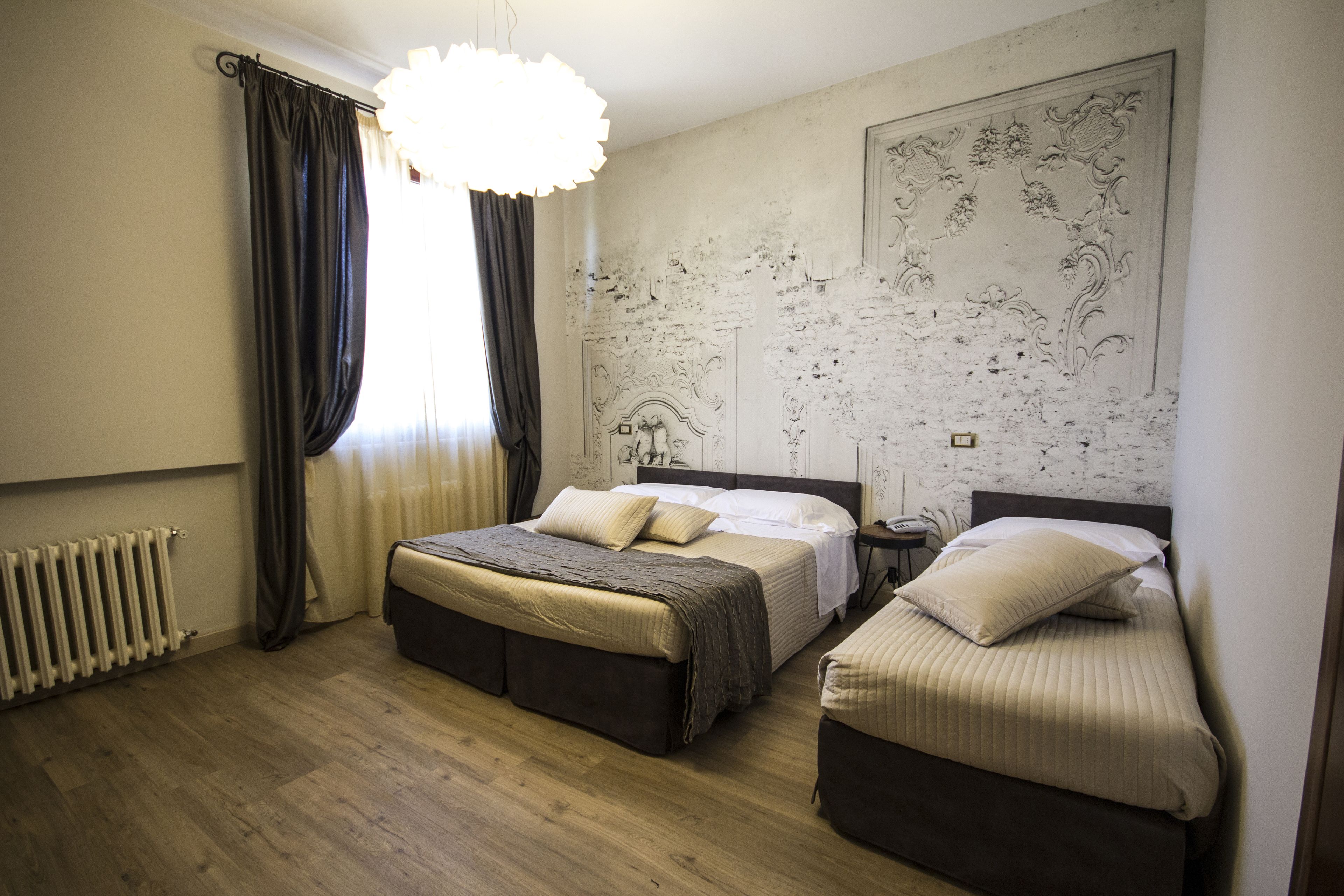 Ein Hotelzimmer mit zwei Betten, einem Heizkörper, einem Fenster mit Vorhängen und einer Wandverzierung.