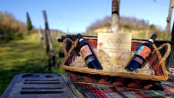 Una cesta de mimbre con dos botellas de vino y una etiqueta que dice “Fodere della Bruciata Toscana” sobre una manta a cuadros.