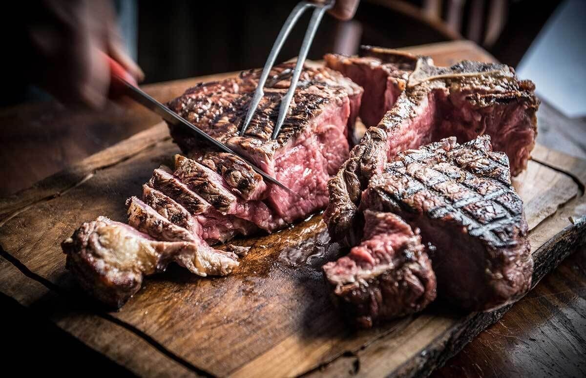 Ein Steak wird auf einem Holztisch angeschnitten.