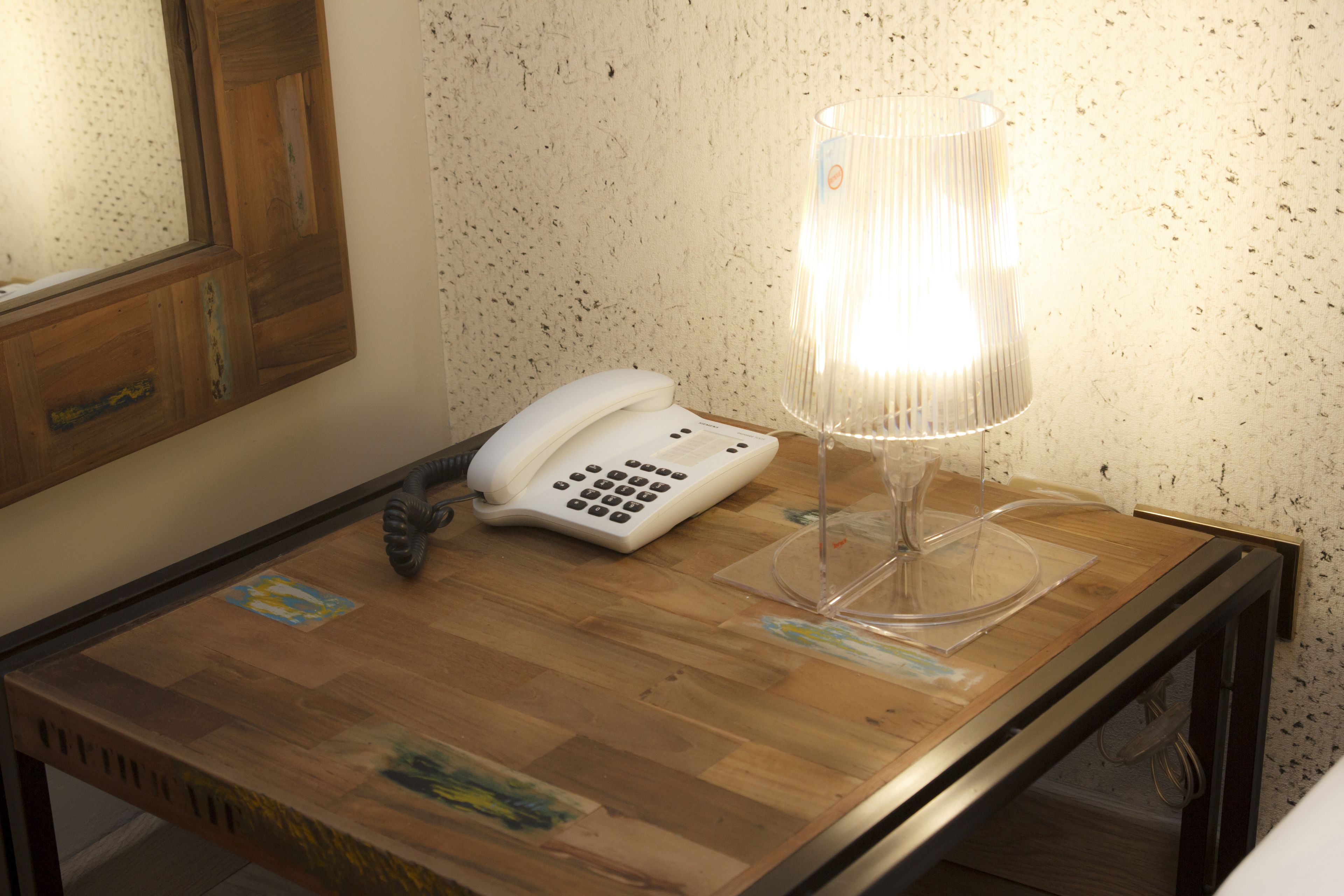 Una mesa de madera con un teléfono blanco y una lámpara de cristal transparente.