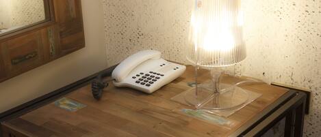 Una mesa de madera con un teléfono blanco y una lámpara de cristal transparente.