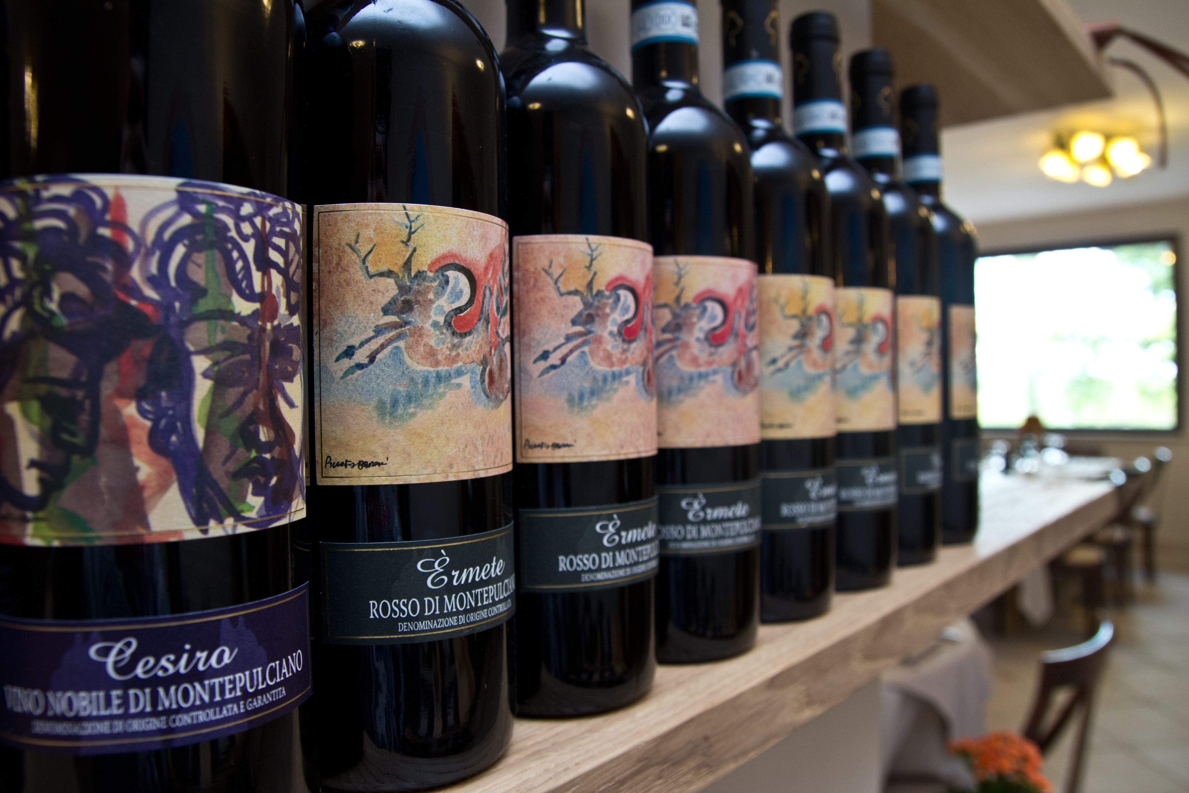 A row of wine bottles with labels on a wooden shelf in a restaurant.