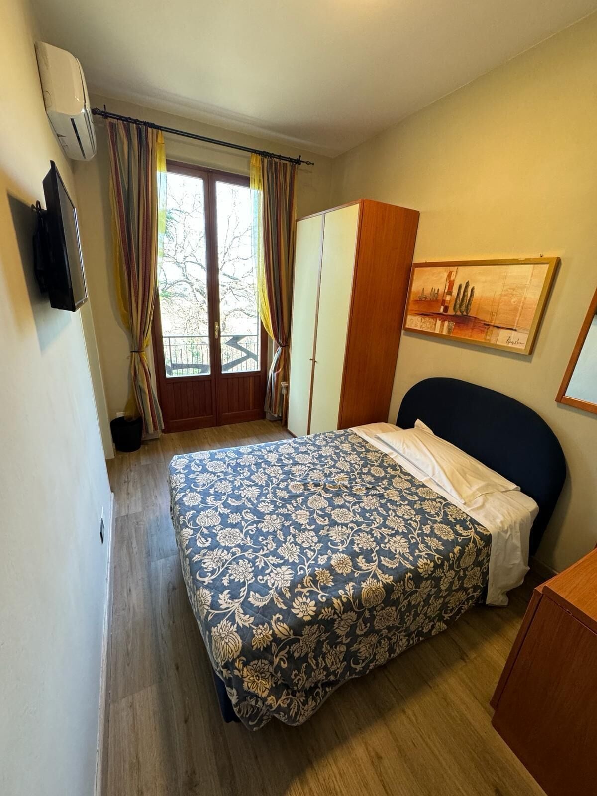 Une chambre à coucher avec un lit, une armoire, un tableau au mur et une fenêtre avec des rideaux.