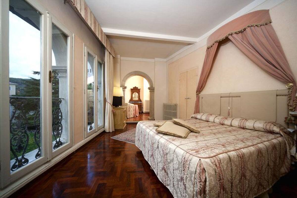 Un dormitori amb un llit gran, una porta corredissa de vidre que dona a un balcó i una porta d'arc clàssic.