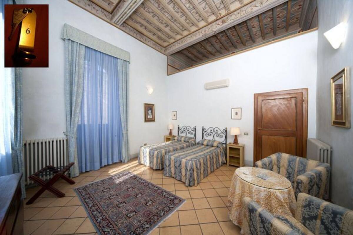 Un dormitori amb dos llits, una taula rodona, una cadira, un radiador i una porta de fusta.