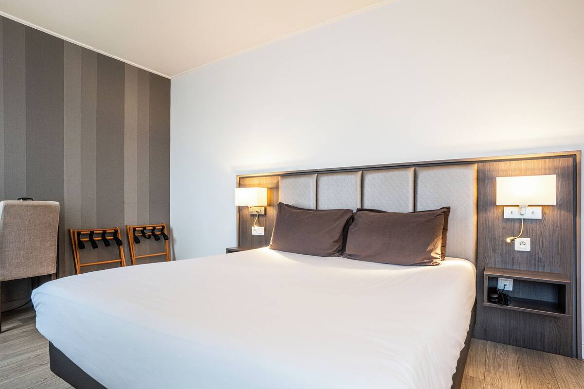 A hotel room with a large bed, two bedside tables with lamps, a chair, and a striped wall.