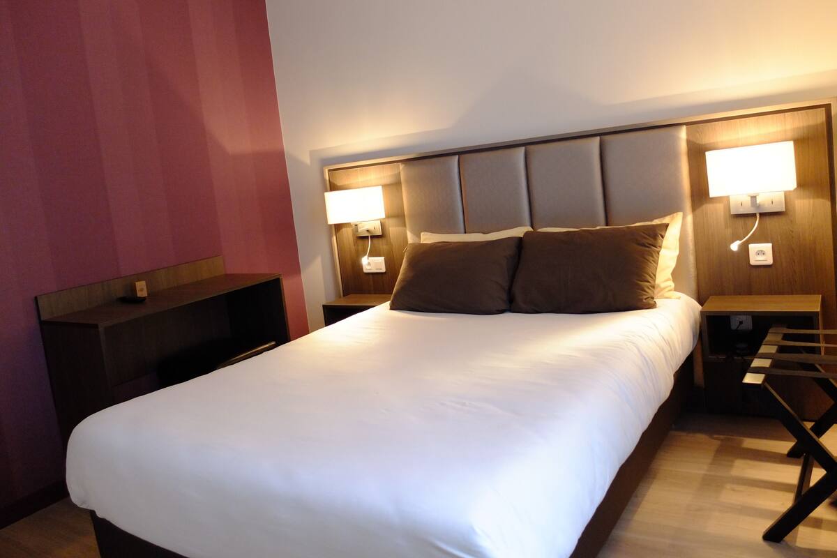 A hotel room with a large bed, two bedside tables, and a nightstand with a lamp.
