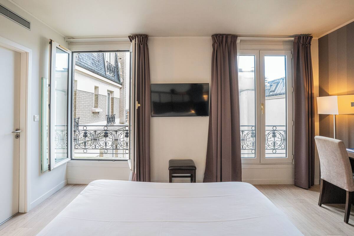 A hotel room with a large bed, a TV mounted on the wall, a small table, and a chair.