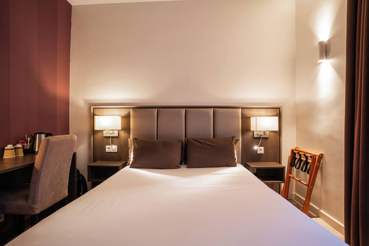 A hotel room with a large bed, two bedside tables with lamps, a chair, and a wooden rack.