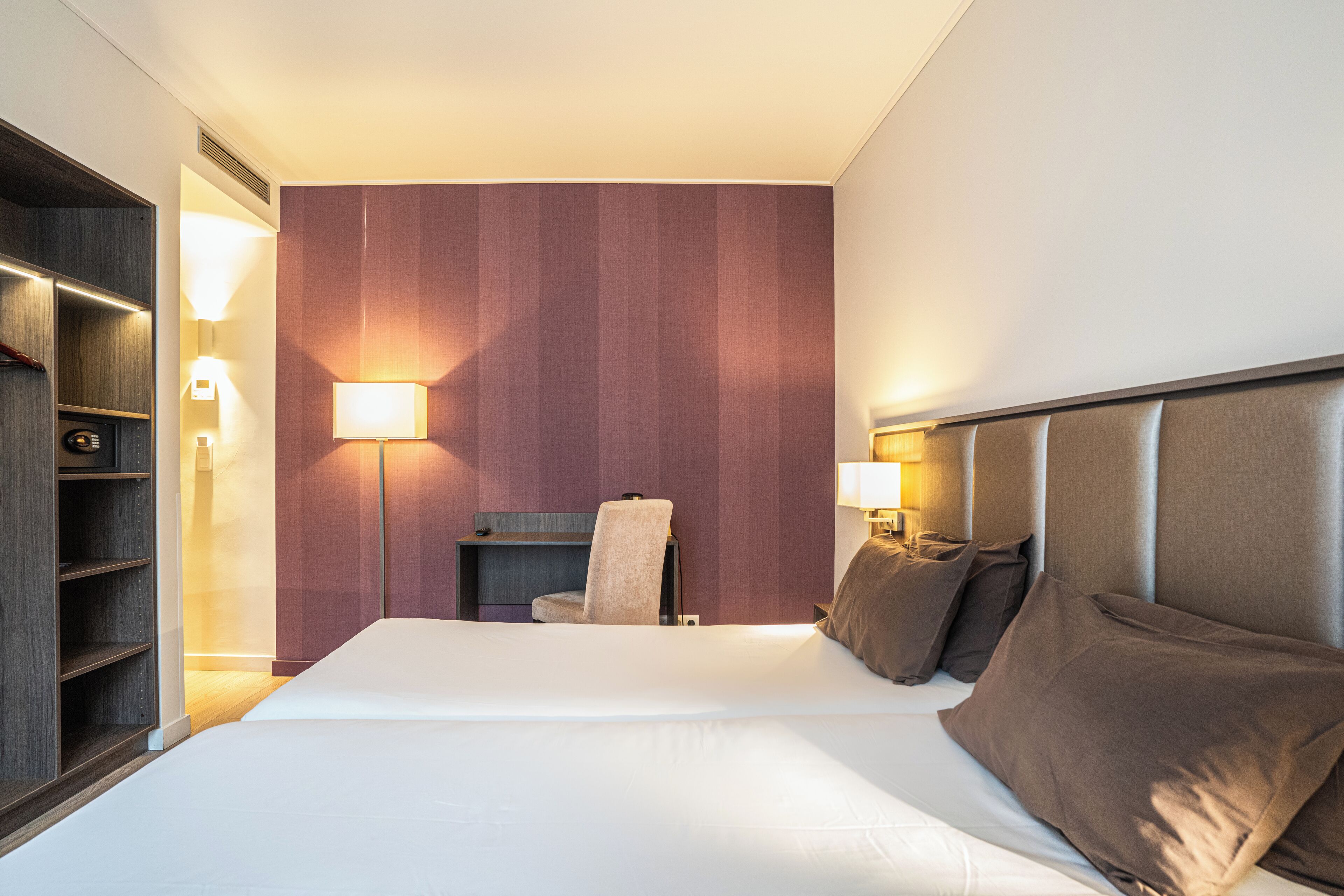Ein Hotelzimmer mit einem großen Bett, einem Sessel, einem Schreibtisch und einem Kleiderschrank.