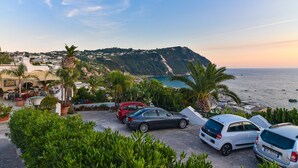 A coastal parking area with cars, lush greenery, and a view of the sea and hills in the background. - Hotel Capizzo (Forio)
