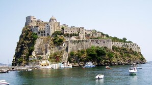 A historic fortified building with multiple levels and a prominent dome, situated on a rocky outcrop by the sea. - Hotel Capizzo (Forio)