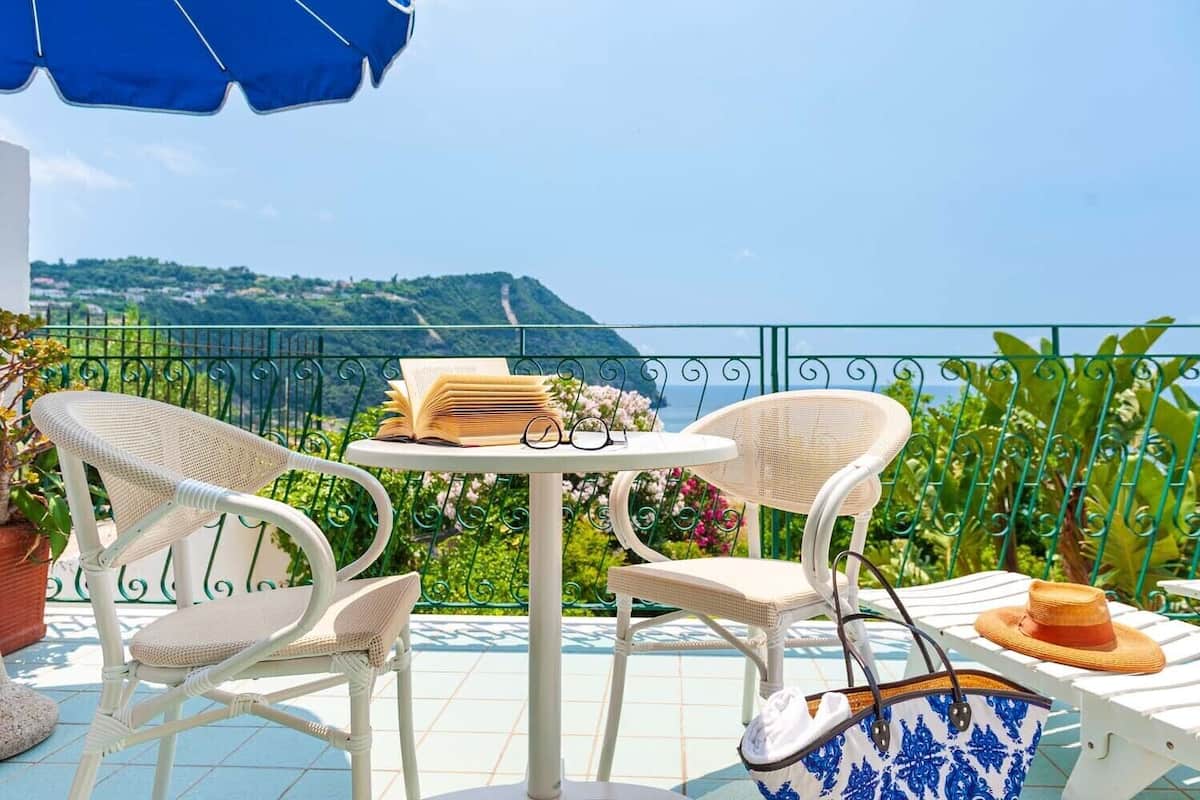 A balcony with two wicker chairs, a small round table, and a blue umbrella.