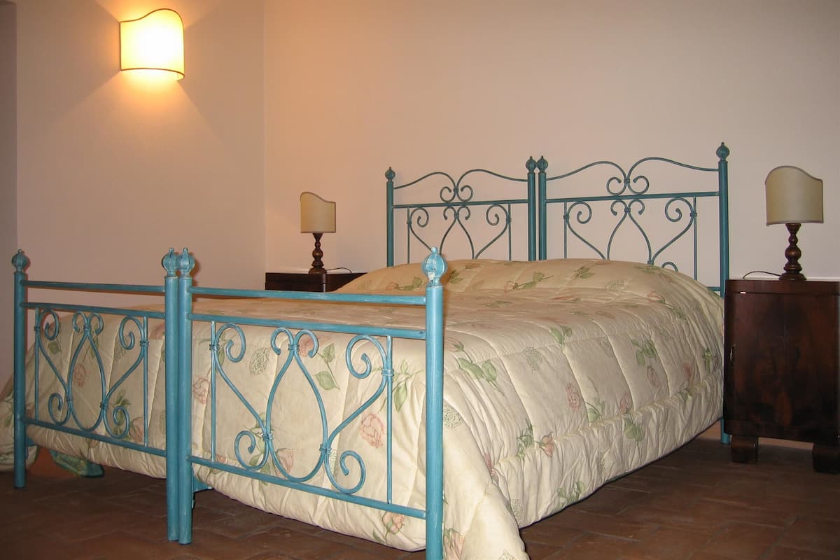Un dormitorio con una cama, dos mesitas de noche, una lámpara de pared y un cabecero decorativo de metal.