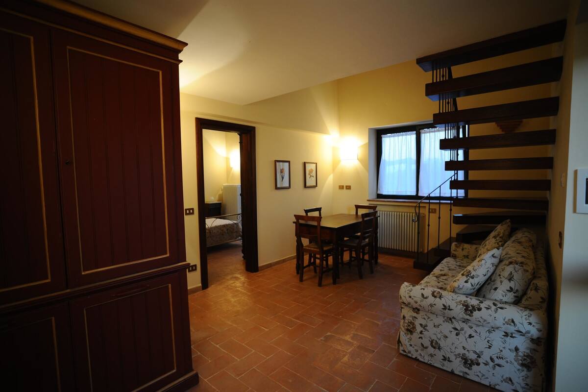 Una sala de estar con un sofá, una mesa de comedor con sillas, una escalera y un armario de madera.