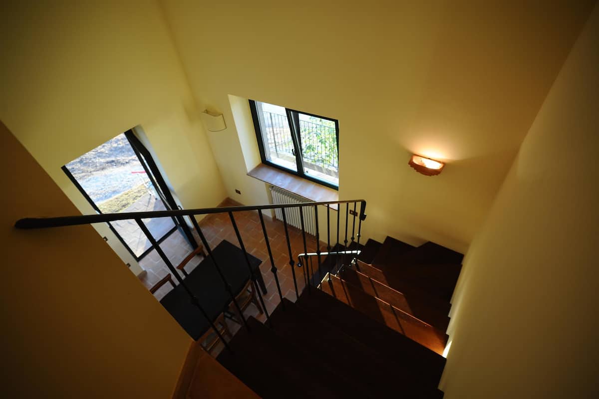 Una escalera con barandilla, una ventana con vista al exterior y un aplique de pared.