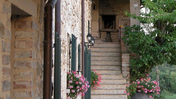 Un edificio de piedra con una escalera de ladrillo que lleva a una puerta. Hay macetas con flores rosadas en los escalones.