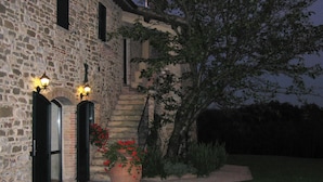 Un edificio de piedra con dos ventanas iluminadas y una planta en maceta con flores rojas.