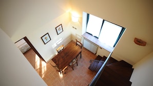 Un comedor con una mesa y sillas de madera, una lámpara fijada a la pared y un ventanal que deja entrar luz natural.