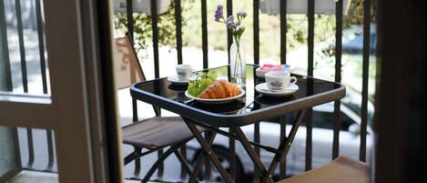 A balcony with a table set for two, featuring a croissant, a vase with flowers, and two cups.