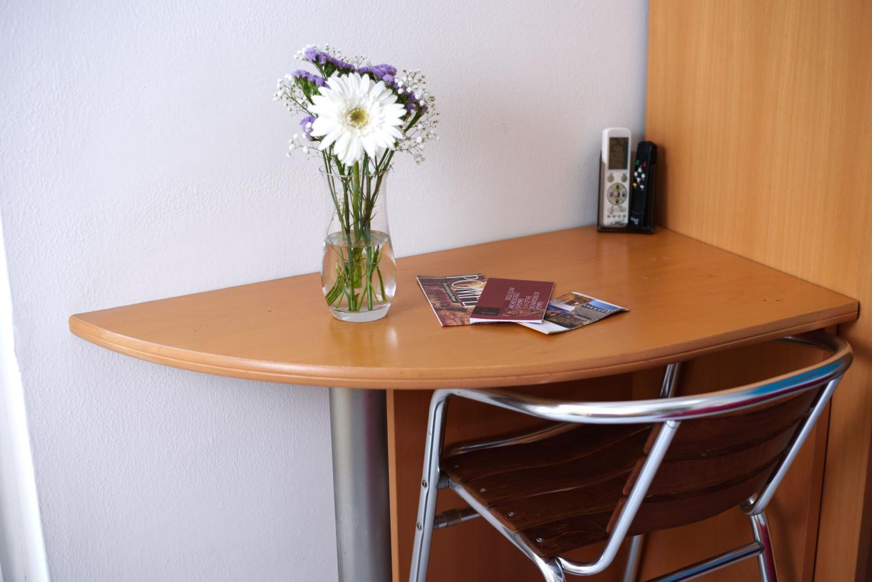 Une petite table sur laquelle se trouvent un vase de fleurs, une télécommande et un magazine.