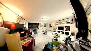 A modern living room with a sofa, chairs, a coffee table, and a TV. There are books and magazines on the table, and a plant in the corner. - Calypso (Pompei)