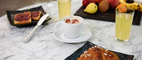 Un desayuno con tostadas, un croissant, una taza de café y un plato de fruta sobre una mesa de mármol.