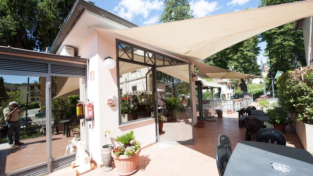 An outdoor patio area with a covered seating area, potted plants, and a reception desk. - Hotel Athena (Spoleto)