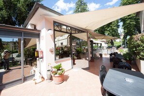An outdoor patio area with a covered seating area, potted plants, and a reception desk. - Hotel Athena (Spoleto)