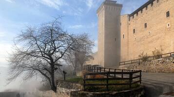 A historic stone building with a tall tower, a paved pathway, and a leafless tree.