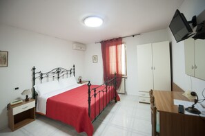 Un dormitorio con cama, escritorio, armario, televisor y ventana con cortinas.